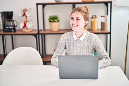 Téléchargez les photos : Jeune femme blonde utilisant un ordinateur portable assis sur la table à manger - en image libre de droit