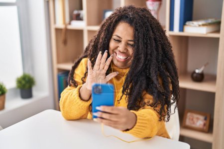 Photo for Plus size hispanic woman using smartphone sitting on the table looking positive and happy standing and smiling with a confident smile showing teeth - Royalty Free Image