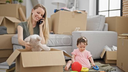 Foto de Madre e hija embalando juguetes en una caja de cartón hablando en un teléfono inteligente en un nuevo hogar - Imagen libre de derechos