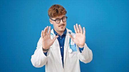 Photo for Young hispanic man doctor standing with serious expression doing calm gesture over isolated blue background - Royalty Free Image