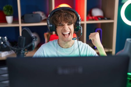 Téléchargez les photos : Jeune homme hispanique jouant à des jeux vidéo criant fier, célébrant la victoire et le succès très excité avec le bras levé - en image libre de droit