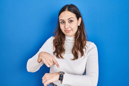 Téléchargez les photos : Jeune femme hispanique debout sur fond bleu à la hâte pointant pour regarder le temps, l'impatience, bouleversé et en colère pour retard de délai - en image libre de droit
