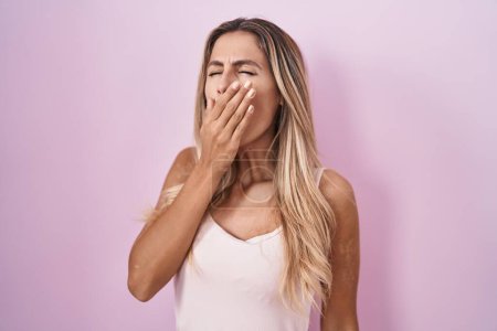 Foto de Young blonde woman standing over pink background bored yawning tired covering mouth with hand. restless and sleepiness. - Imagen libre de derechos