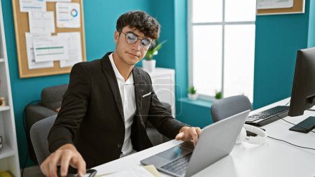 Foto de Adolescente hispano serio y joven que adopta la tecnología y trabaja como profesional de negocios en la oficina. sentado en su escritorio, investido de éxito, se sumerge en el trabajo en su computadora portátil - Imagen libre de derechos