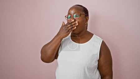 Foto de Mujer afroamericana agotada con trenzas bostezando, ojos cansados detrás de las gafas. de pie casualmente sobre el fondo aislado rosa, expresión seria pero relajada. - Imagen libre de derechos