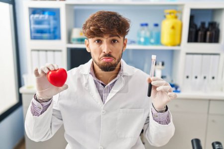 Photo for Arab man with beard working at scientist laboratory holding blood samples depressed and worry for distress, crying angry and afraid. sad expression. - Royalty Free Image