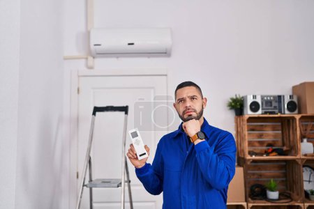 Photo for Hispanic repairman working with air conditioner serious face thinking about question with hand on chin, thoughtful about confusing idea - Royalty Free Image