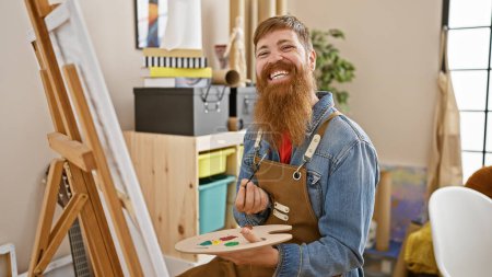 Photo for Smiling young redhead man radiating confidence, drawing away blissfully at art studio, an indoor setting sparkling with creativity. - Royalty Free Image
