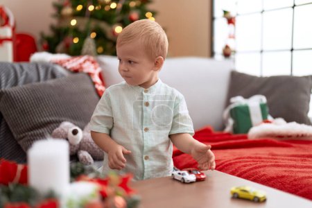 Foto de Adorable niño jugando con juguete de coche de pie junto al árbol de Navidad en casa - Imagen libre de derechos
