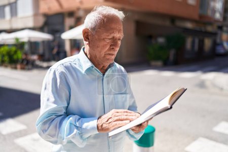 Photo for Middle age grey-haired man reading book at street - Royalty Free Image