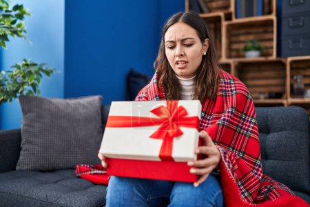 Photo for Young hispanic woman opening gift box clueless and confused expression. doubt concept. - Royalty Free Image