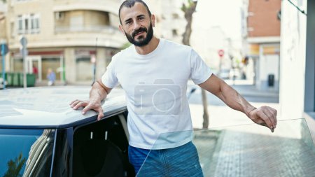 Téléchargez les photos : Jeune homme hispanique souriant confiant debout en voiture à la rue - en image libre de droit