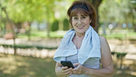 Foto de Mujer de mediana edad usando teléfono inteligente sonriendo en el parque - Imagen libre de derechos