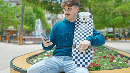 Téléchargez les photos : Jeune homme hispanique tenant le patin à l'aide d'un smartphone au parc - en image libre de droit