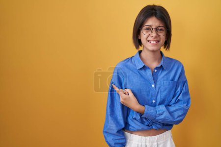 Photo for Young girl standing over yellow background pointing aside worried and nervous with forefinger, concerned and surprised expression - Royalty Free Image