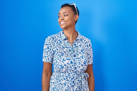 Téléchargez les photos : Femme afro-américaine debout sur fond bleu regardant de côté avec le sourire sur le visage, expression naturelle. riant confiant. - en image libre de droit