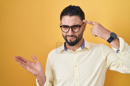 Photo for Hispanic young man wearing business clothes and glasses confused and annoyed with open palm showing copy space and pointing finger to forehead. think about it. - Royalty Free Image