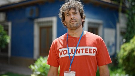 Téléchargez les photos : Jeune activiste hispanique portant un uniforme de bénévole debout avec un visage sérieux au parc - en image libre de droit