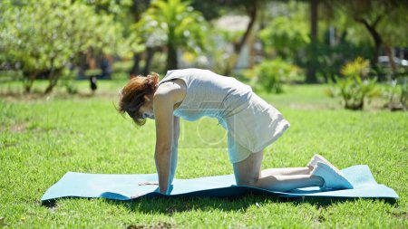 Foto de Mujer de mediana edad que se extiende de nuevo en la estera de yoga en el parque - Imagen libre de derechos