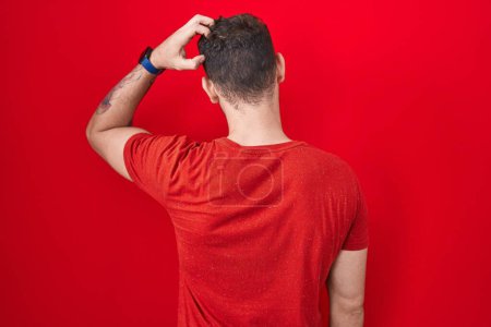 Foto de Young hispanic man standing over red background backwards thinking about doubt with hand on head - Imagen libre de derechos