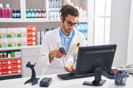 Foto de Joven hombre hispano farmacéutico escaneando pastillas botella en la farmacia - Imagen libre de derechos