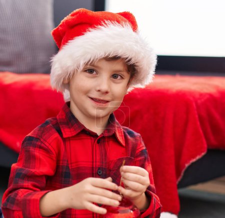Foto de Adorable niño hispano sonriendo confiado sosteniendo la decoración de la bola de Navidad en casa - Imagen libre de derechos