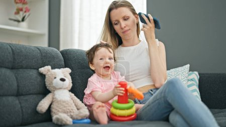 Photo for Mother and daughter listening to voice message by smartphone while playing with hoops at home - Royalty Free Image