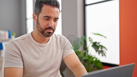 Téléchargez les photos : Jeune homme hispanique utilisant un ordinateur portable assis sur la table à la salle à manger - en image libre de droit