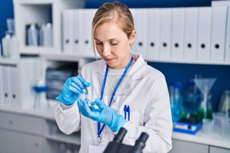 Foto de Joven mujer rubia científica sosteniendo pastillas en el laboratorio - Imagen libre de derechos