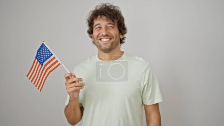 Téléchargez les photos : Jeune homme hispanique souriant confiant tenant drapeau des États-Unis sur fond blanc isolé - en image libre de droit