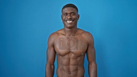 Téléchargez les photos : Afro-américain homme souriant confiant debout torse nu sur fond bleu isolé - en image libre de droit