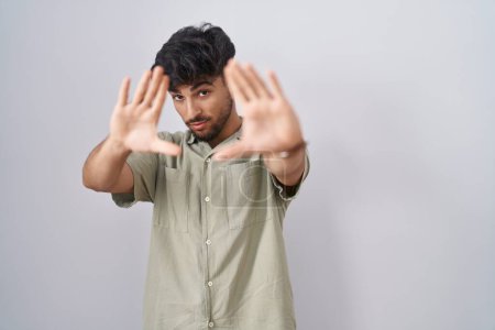 Téléchargez les photos : Homme arabe avec barbe debout sur fond blanc faisant cadre en utilisant les mains paumes et les doigts, perspective de la caméra - en image libre de droit