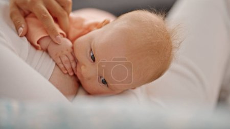 Photo for Mother and daughter sitting on sofa breastfeeding baby at home - Royalty Free Image