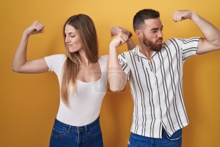 Téléchargez les photos : Jeune couple debout sur fond jaune montrant les muscles des bras souriant fier. concept de fitness. - en image libre de droit