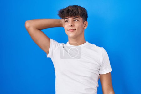 Photo for Hispanic teenager standing over blue background smiling confident touching hair with hand up gesture, posing attractive and fashionable - Royalty Free Image