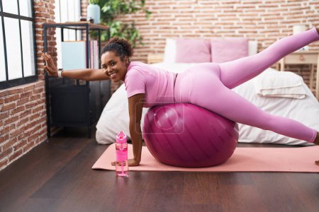 Photo for African american woman training legs exercise using fit ball at bedroom - Royalty Free Image