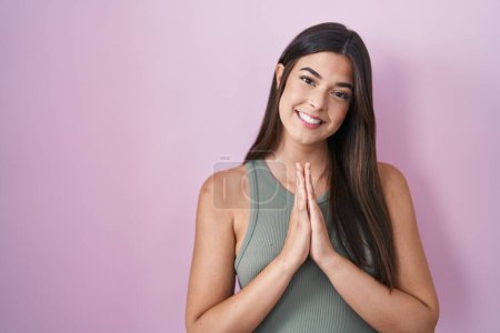 Téléchargez les photos : Hispanic woman standing over pink background praying with hands together asking for forgiveness smiling confident. - en image libre de droit