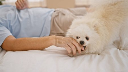 Photo for Relaxed morning scenario with handsome young caucasian man, effortlessly chilling with his loyal dog lying on the comfortable bed in bedroom. loving the expressively playful, indoor lifestyle. - Royalty Free Image