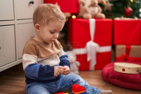Téléchargez les photos : Adorable tout-petit jouant avec des blocs de construction assis sur le sol par des cadeaux de Noël à la maison - en image libre de droit
