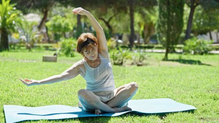 Photo for Middle age woman sitting on yoga mat training at park - Royalty Free Image