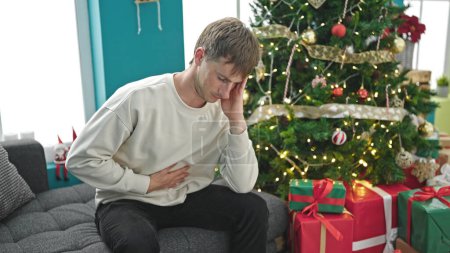 Téléchargez les photos : Jeune homme caucasien souffrant de maux d'estomac célébrant Noël à la maison - en image libre de droit