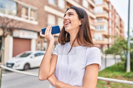 Téléchargez les photos : Jeune belle femme hispanique souriant confiant écoute message audio par le smartphone à la rue - en image libre de droit