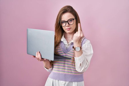 Téléchargez les photos : Young caucasian woman working using computer laptop showing middle finger, impolite and rude fuck off expression - en image libre de droit