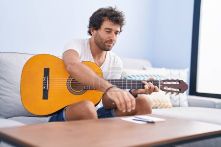 Foto de Young hispanic man playing classical guitar composing song at home - Imagen libre de derechos