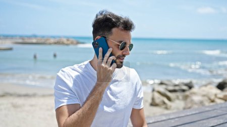Photo for Young hispanic man smiling confident talking on the smartphone at seaside - Royalty Free Image