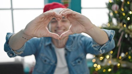 Téléchargez les photos : Jeune homme hispanique célébrant Noël en forme de cœur avec les mains à la maison - en image libre de droit