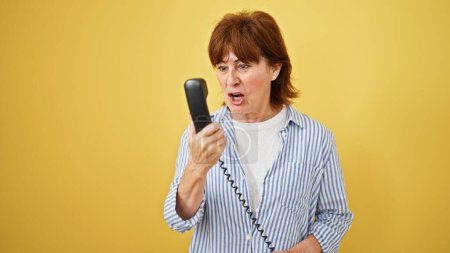 Foto de Mujer de mediana edad hablando por teléfono discutiendo sobre el fondo amarillo aislado - Imagen libre de derechos