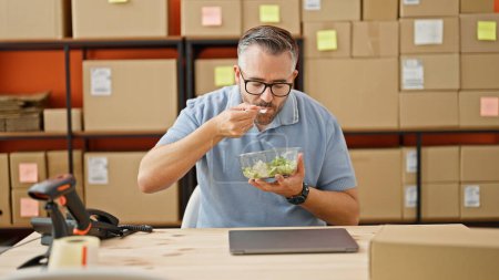 Photo for Grey-haired man ecommerce business eating salad at office - Royalty Free Image