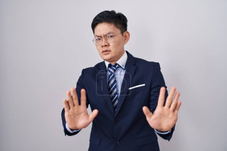 Photo for Young asian man wearing business suit and tie moving away hands palms showing refusal and denial with afraid and disgusting expression. stop and forbidden. - Royalty Free Image