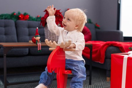 Foto de Adorable niño rubio jugando con el rockeo de renos por la decoración de Navidad en casa - Imagen libre de derechos